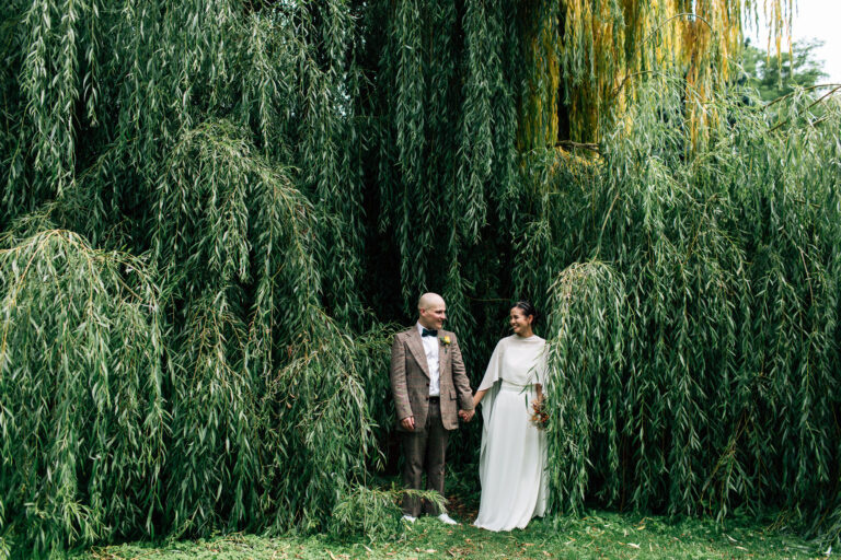 Couple taking wedding photo by old willow tree at Ashbridge Estate